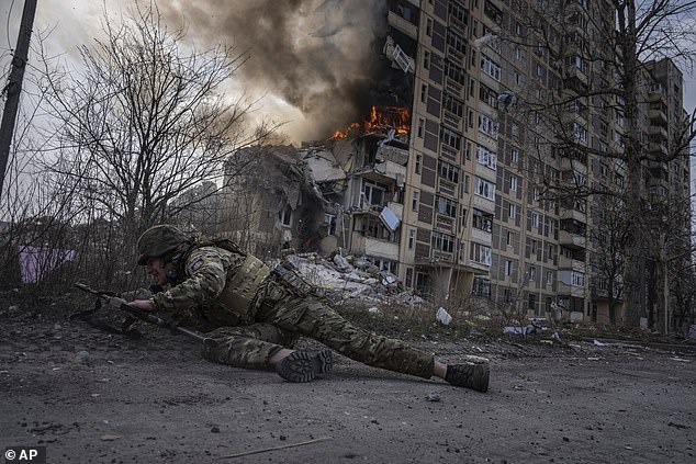 A Ukrainian police officer takes cover in front of a burning building hit in a Russian airstrike in Avdiivka, Ukraine, on Friday