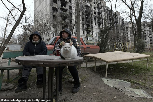 Residents are seen outside damaged buildings with a cat as the Russo-Ukrainian war rages on in Mariupol's Russian-controlled territory of Ukraine